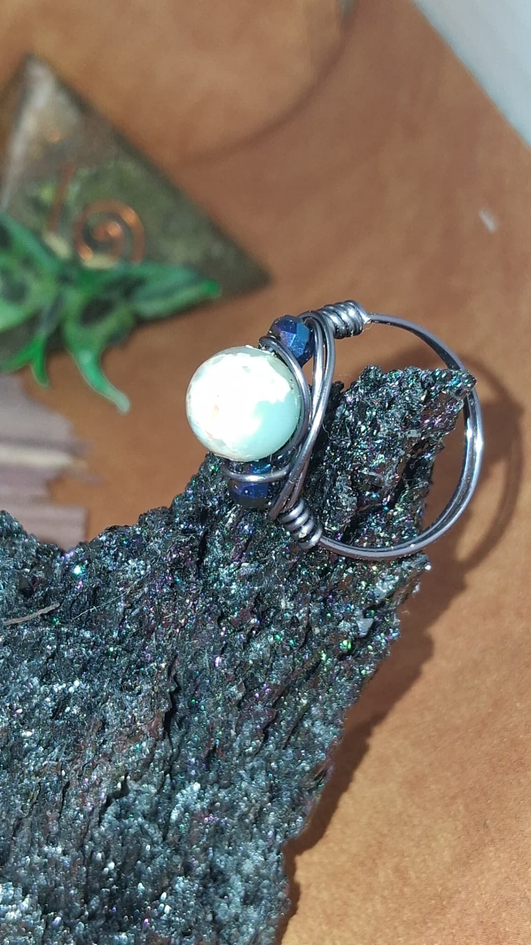 Close-up of a wire-wrapped ring with a pale stone bead and deep blue accents, resting on a dark crystal