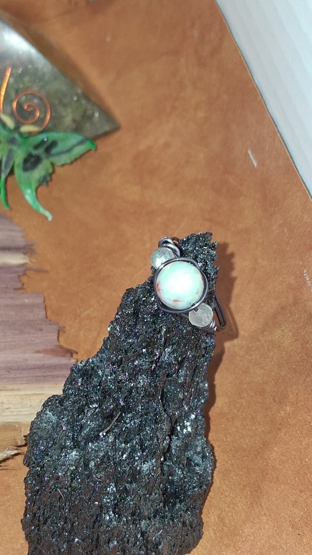 A wire-wrapped ring with a pale stone bead displayed on a piece of sparkling dark stone